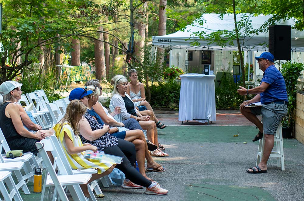 An author speaks to an audience in an outdoor setting