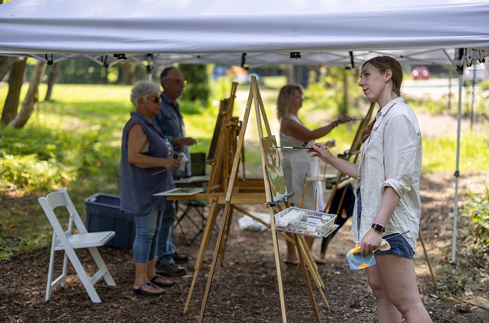 Four artists paint at easels under a tent